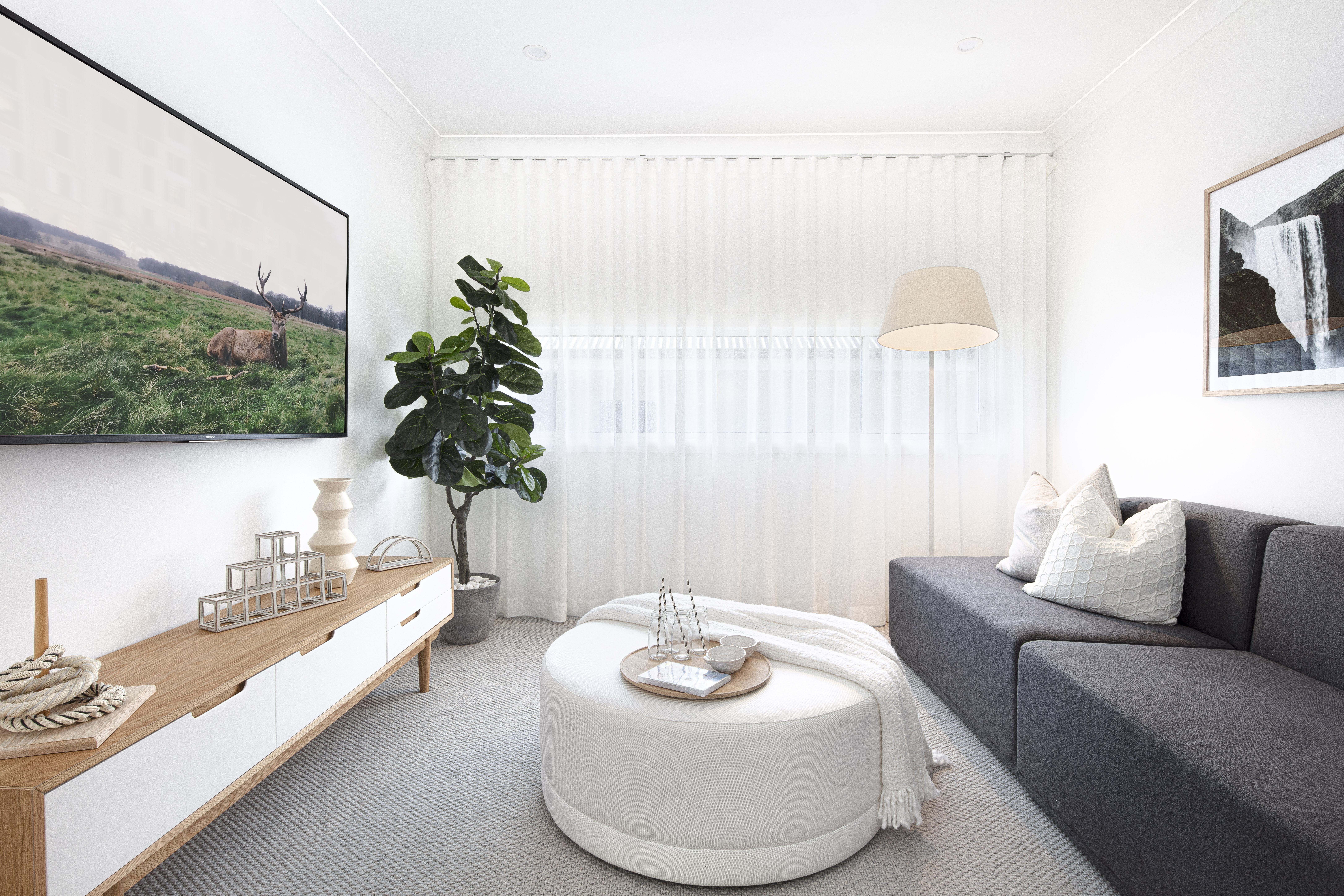 Theatre room with wall length couch opposite low TV unit and wall mounted TV