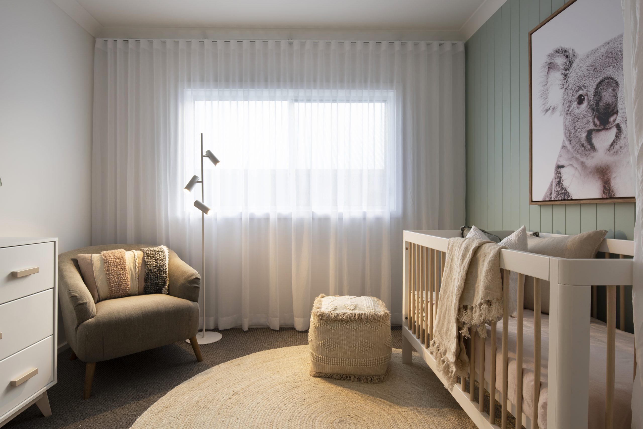 A bedroom styled as a nursery in the Avalon 220 display home with crib below a wall mounted painting of a koala