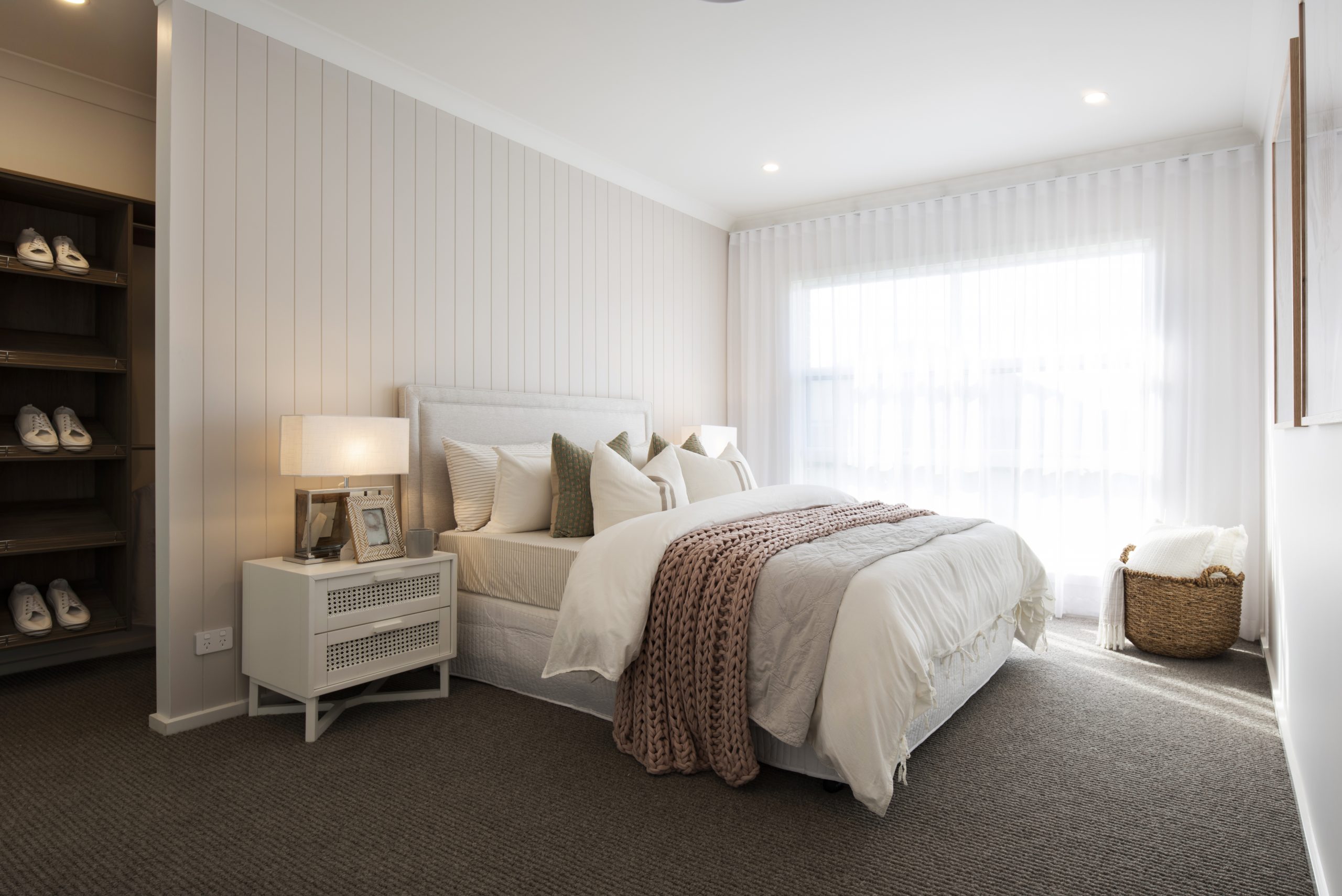 Master bedroom in the Avalon 220 display home with apolstered bed against a blush panneled wall that shows a left hand side opening to the wardrobe