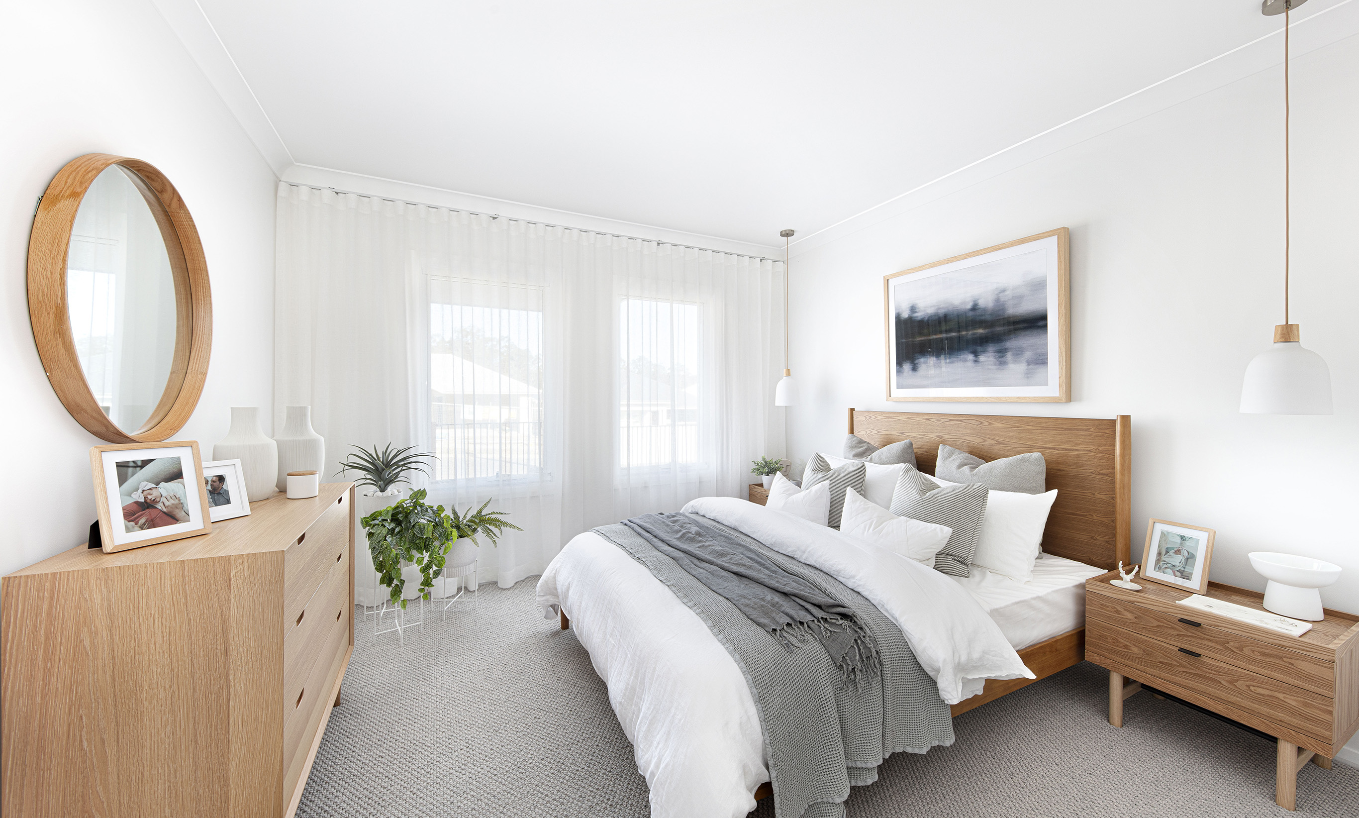 Side on view of the master bedroom in the Lucia One display home with wooden bed and bedsides opposite 6 drawer dresser and parallel to windows covered by floor to ceiling curtains