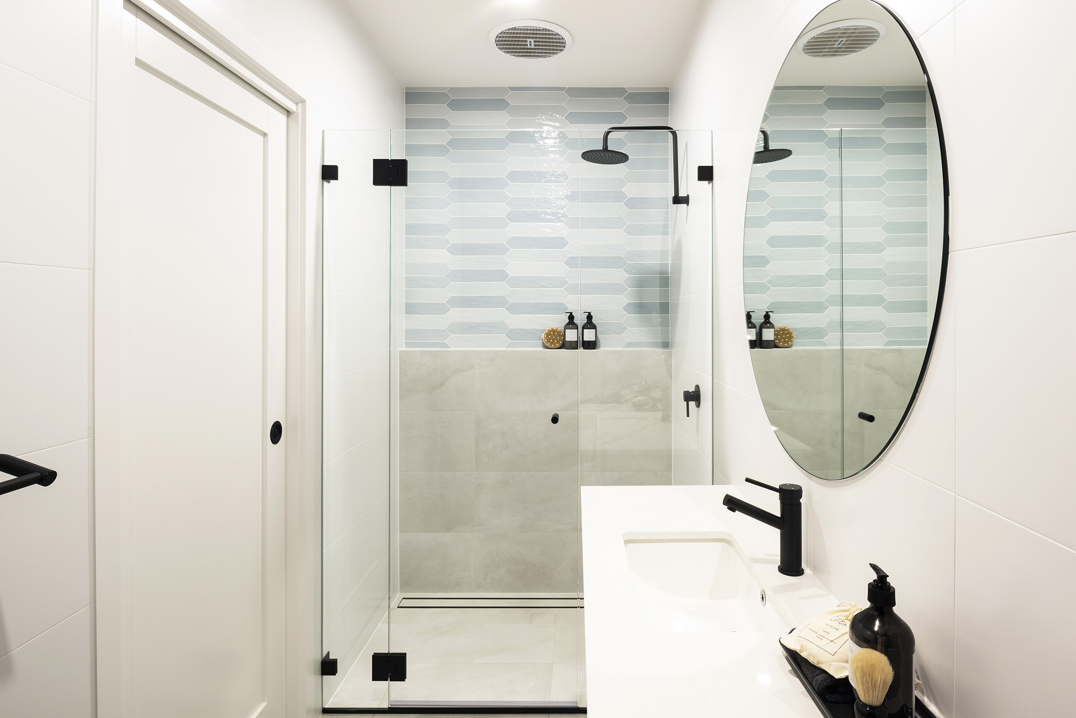 View of a right hand sided single sink below a circular mirror and facing the shower in the Avoca display home