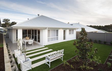 Backyard of the Avoca display home featuring grassed area, wooden bench overlooking stoned pavers and facing a larger paved dining area