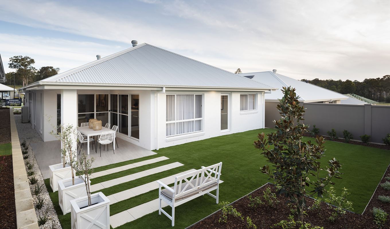 Backyard of the Avoca display home featuring grassed area, wooden bench overlooking stoned pavers and facing a larger paved dining area